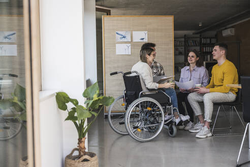 Junge Geschäftsleute bei einem Treffen im Büro mit einer Frau, die im Rollstuhl sitzt - UUF25711