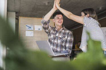 Happy young businessman and businesswoman high fiving in office - UUF25724