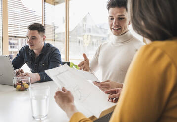 Junge Geschäftsleute besprechen ein Dokument während einer Sitzung im Büro - UUF25737