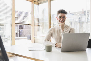 Smiling young businessman using laptop at desk in office - UUF25742