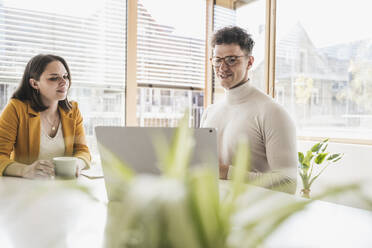 Young businessman and businesswoman sitting at desk in office - UUF25746