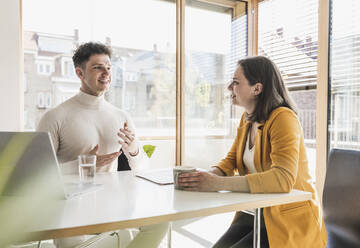 Young businessman and businesswoman talking at desk in office - UUF25747