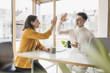 Young businessman and businesswoman high fiving in office - UUF25748
