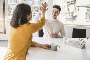 Young businessman and businesswoman high fiving in office - UUF25749