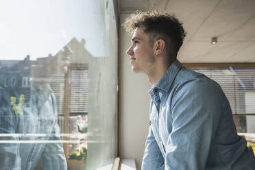 Junger Geschäftsmann schaut im Büro aus dem Fenster - UUF25756