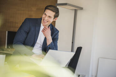 Happy businessman using laptop in office - UUF25779