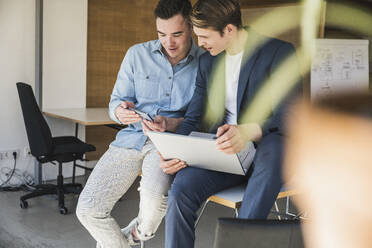 Zwei Kollegen teilen sich ein Smartphone im Büro - UUF25787