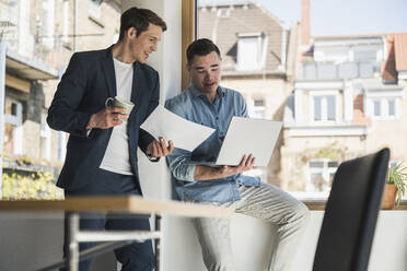 Two happy colleagues with laptop and documents in office - UUF25790