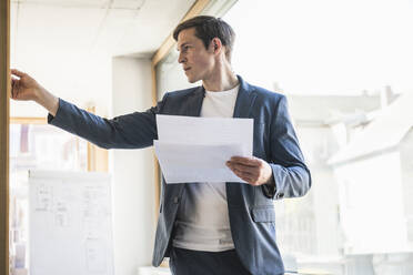 Businessman holding documents working on strategy in office - UUF25796