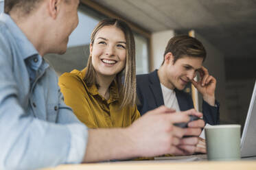 Smiling business people with smartphone and laptop in office - UUF25821