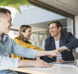 Happy business team touching fists in office - UUF25826