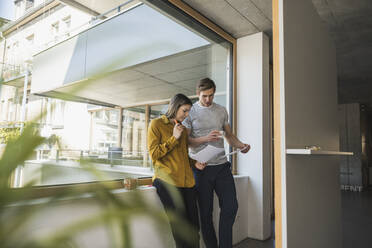 Businessman and businesswoman discussing documents at the window in office - UUF25827