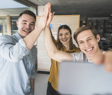 Happy business people high fiving and taking a selfie in office - UUF25848