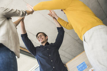 Happy business people standing together with raised arms in office - UUF25855