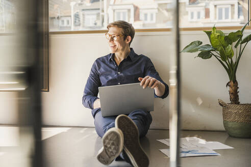 Geschäftsmann sitzt auf dem Boden im Büro und benutzt einen Laptop - UUF25860