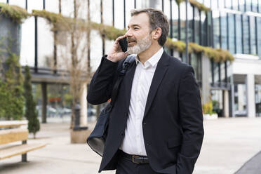 Businessman talking on smart phone standing outside office building - OIPF01509