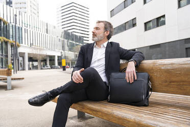 Älterer Geschäftsmann mit Laptoptasche auf einer Bank vor einem Bürogebäude sitzend - OIPF01511