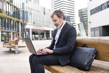 Älterer Geschäftsmann mit Laptop auf einer Bank sitzend - OIPF01513