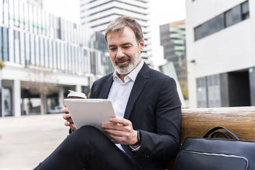 Businessman holding disposable coffee cup using tablet PC sitting on bench - OIPF01518