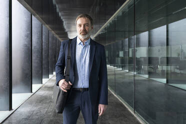 Mature businessman with laptop bag standing in corridor - OIPF01532