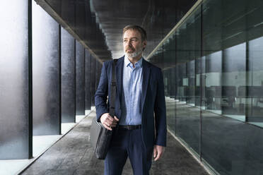 Businessman with laptop bag standing in corridor - OIPF01533