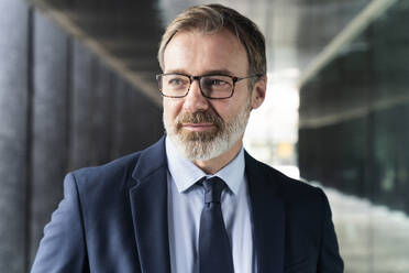 Mature businessman wearing eyeglasses standing in corridor - OIPF01544