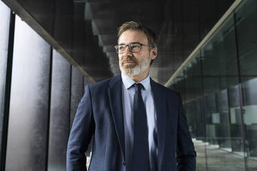 Businessman in suit wearing eyeglasses standing in corridor - OIPF01545