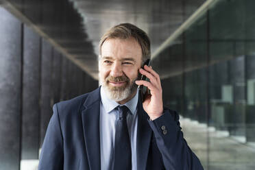 Smiling businessman talking on smart phone in corridor - OIPF01547