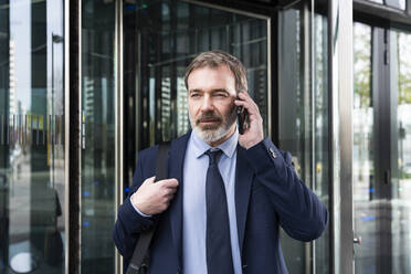 Businessman talking on smart phone outside office building - OIPF01564