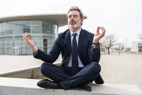 Mature businessman with eyes closed meditating sitting on wall - OIPF01572