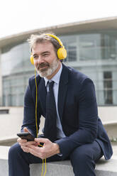 Smiling businessman listening music on headphones - OIPF01575