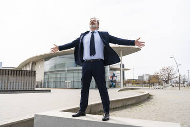 Carefree businessman with arms outstretched standing on wall at office park - OIPF01577