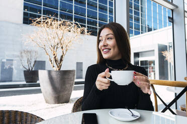Glückliche Geschäftsfrau mit Kaffeetasse am Tisch im Café sitzend - PNAF03741