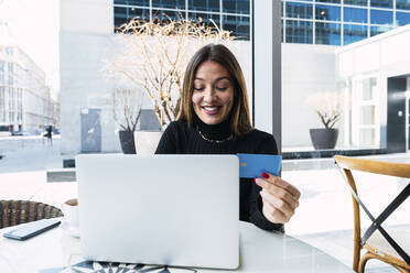 Glückliche Geschäftsfrau mit Kreditkarte und Laptop in einem Café sitzend - PNAF03749