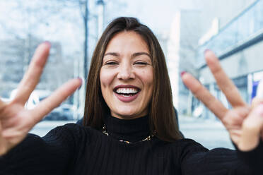 Cheerful young woman gesturing peace sign - PNAF03772