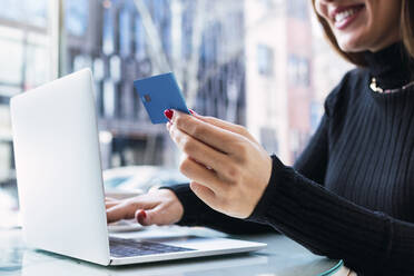 Smiling businesswoman sitting with laptop holding credit card - PNAF03777