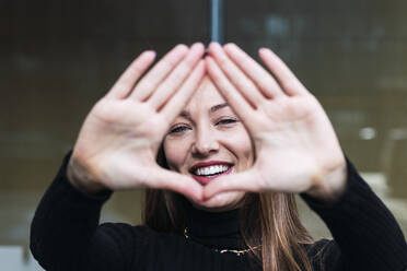 Happy young woman gesturing finger frame - PNAF03785