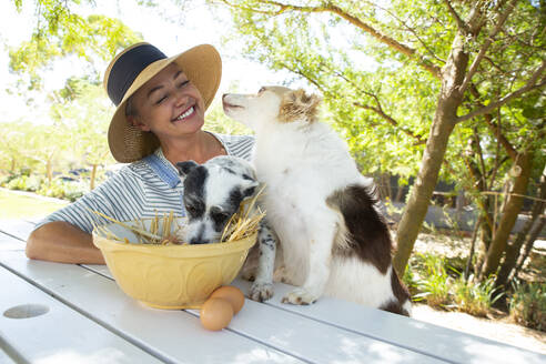 Happy woman with dogs sitting at table in garden - ESTF00012