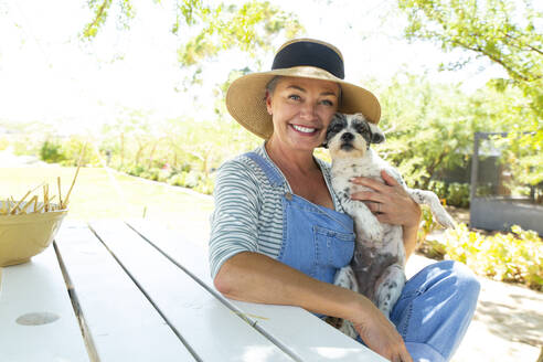 Smiling woman with dog sitting at table in garden - ESTF00013