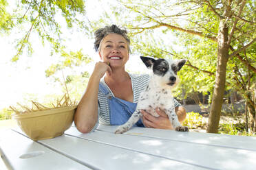 Woman sitting at table with dog in garden - ESTF00014