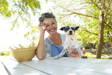 Smiling woman with pet dog at table in garden - ESTF00015