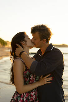 Zärtliches junges Paar küsst sich am Strand an einem sonnigen Tag - SSGF00741