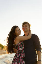 Happy young couple standing at beach on sunny day - SSGF00742