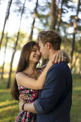 Happy young couple embracing each other in forest - SSGF00748