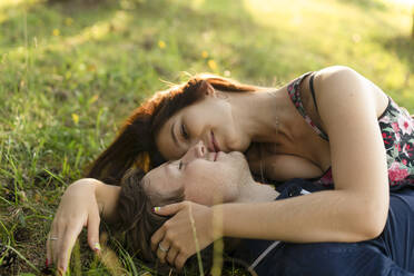 Lächelndes junges Paar im Gras liegend an einem sonnigen Tag - SSGF00757