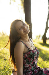 Happy young woman with long hair sitting in nature - SSGF00759