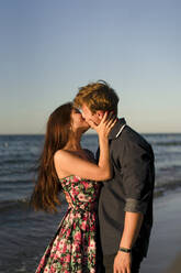 Affectionate couple kissing each other at beach on sunset - SSGF00760