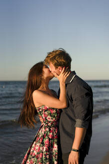 Zärtliches Paar, das sich am Strand bei Sonnenuntergang küsst - SSGF00760