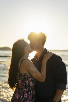 Junges Paar küsst sich an einem sonnigen Tag vor dem Meer - SSGF00762
