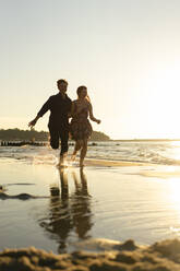 Glückliches junges Paar läuft am Strand an einem sonnigen Tag - SSGF00769